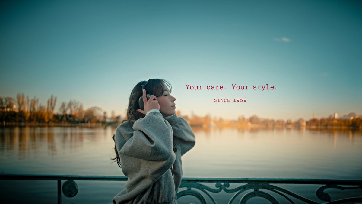 Nainen sillalla kuulokkeet korvilla ja teksti Your care Your style since 1959